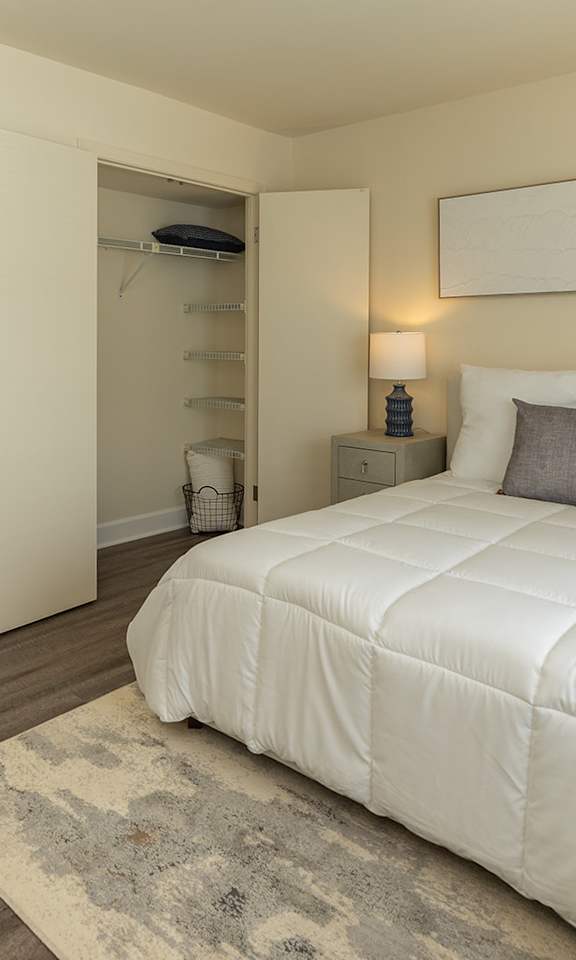 A bedroom with a large bed, two nightstands, and a rug. at The Brittany Apartments, Pikesville, MD, 21208