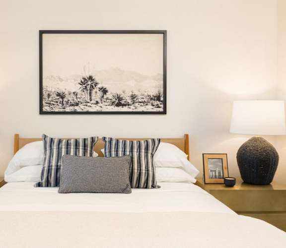a bedroom with a bed with white sheets and pillows and a framed picture above