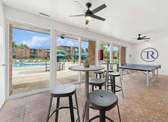 A room with a pool outside the window and a table with chairs.
