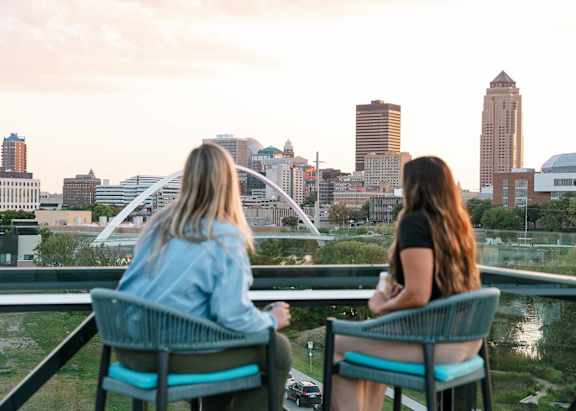 Two women sitting on a balcony overlooking a city skyline.at Level, Des Moines, IA