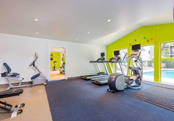 a gym with exercise machines and a pool in the background