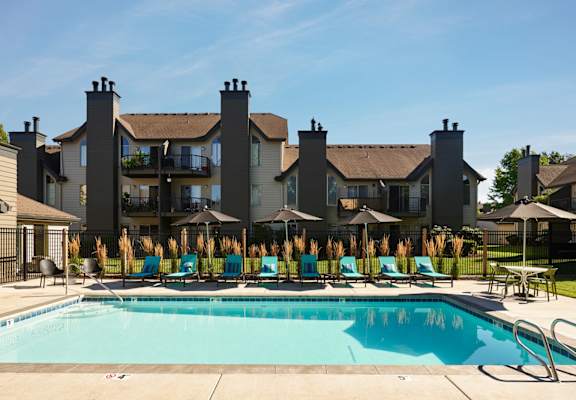 a swimming pool with blue chaise lounge chairs and umbrellas in front of a large