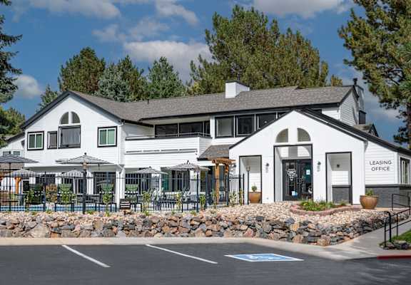 A white building with a black roof and a sign that says "Leasing Office" is in front of some trees.