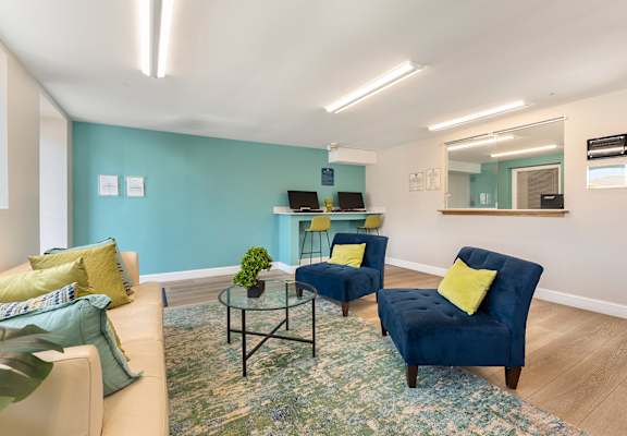 A living room with a blue chair and a glass table.