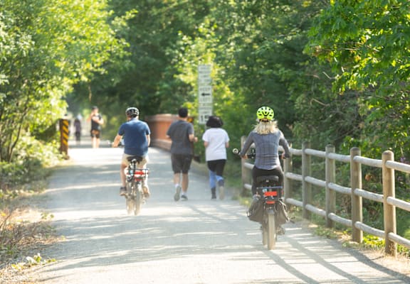 A person on a bicycle is riding down a path with other people walking behind them.