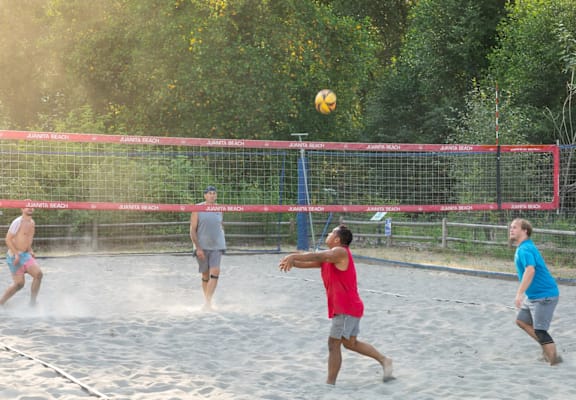A group of people playing volleyball on a sandy court.