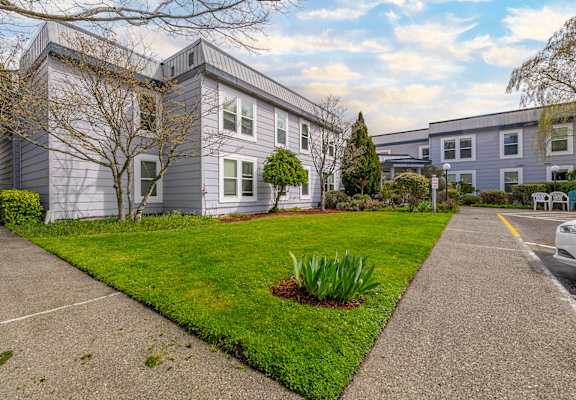 A grey house with a green lawn and a white car parked in front.