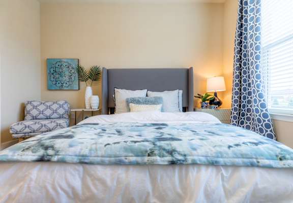 a bedroom with a bed and a chair and a window at The Residences at Bluhawk Apartment Homes, Overland Park, Kansas