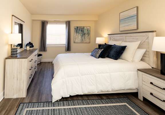 A bedroom with a large bed, a dresser, and a painting on the wall.