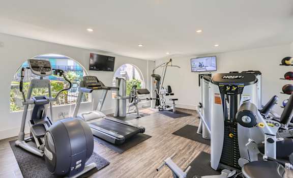 a gym with various machines and televisions on the wall