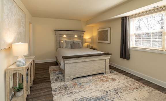 A bedroom with a bed, nightstand, and a rug. at Liberty Gardens Apartments, Baltimore