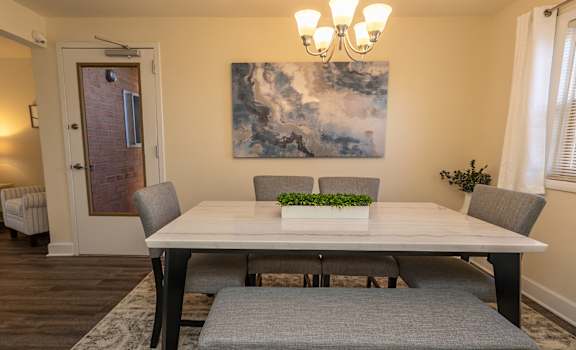 A dining room with a table, chairs, and a painting on the wall. at Liberty Gardens Apartments, Baltimore