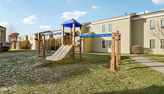 A playground with a yellow slide and a blue canopy is in front of a row of houses. at Forest Apartments, Palmer