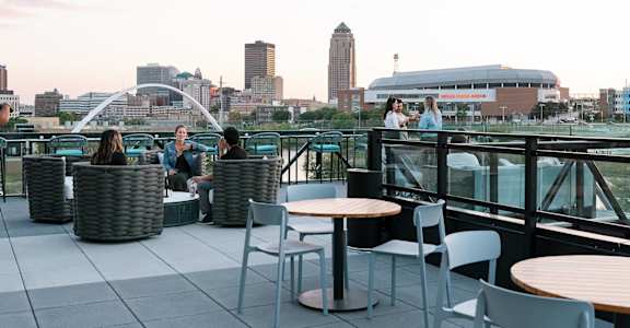 A group of people are sitting on a rooftop terrace with a city skyline in the background.at Level, Des Moines Iowa