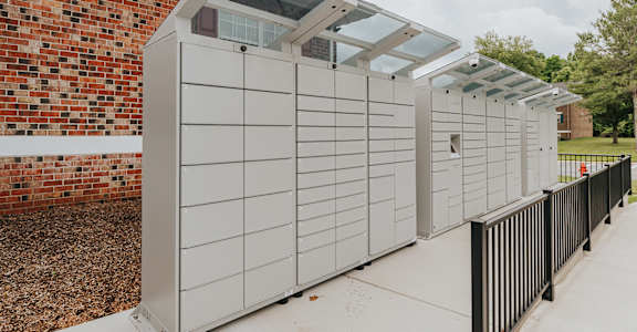 A series of large, white, metal storage units with glass panels on top are lined up on a sidewalk.