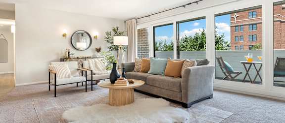 A living room with a grey couch, a white rug, and a round mirror on the wall.