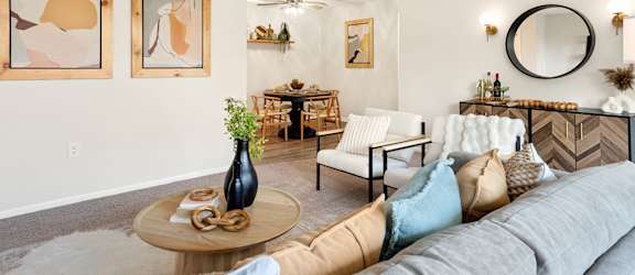 A living room with a grey couch and a round mirror on the wall.