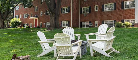 Four white chairs are placed on a lawn in front of a red brick building.