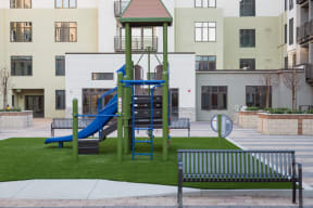 Pet Friendly Apartments in Cupertino CA - Nineteen800 - Playground with Slide, Climbing Equipment, Artificial Grass, Benches, Planters, and View of Apartment Building in the Background at Nineteen800 