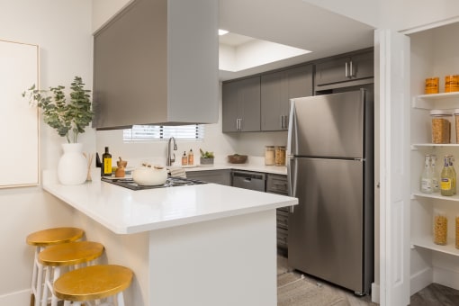 a kitchen with gray cabinets and a white counter top with three stools
