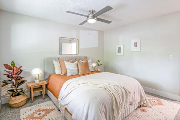 A bedroom with a bed, a ceiling fan, and a potted plant.