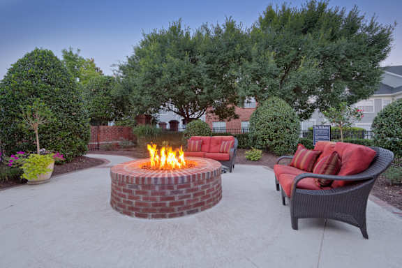 A fire pit in the middle of a patio surrounded by chairs and plants.
