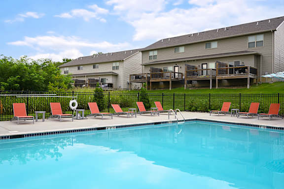 A swimming pool in front of a building with red chairs around it.