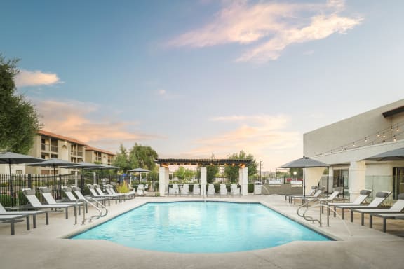 a swimming pool with chaise lounge chairs and umbrellas in front of a building