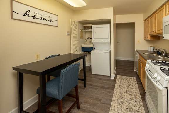 A kitchen with a table and chairs in front of a sign that says Home Sweet Home. at The Brittany Apartments, Maryland