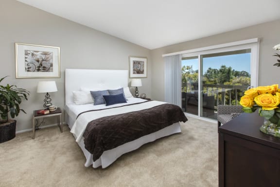 Two-Bedroom Apartments in Dana Pointe, CA - Harbor Pointe - Bedroom with Balcony Access, Carpeting, and Nightstands at Harbor Pointe, Dana Point, CA