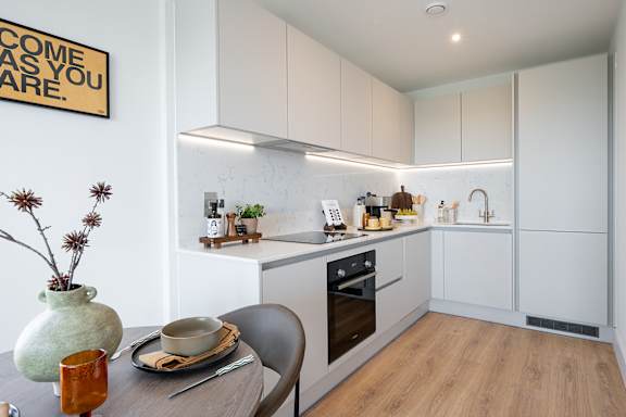 A kitchen with a table set for two and a sign on the wall that says "Welcome as you are.".