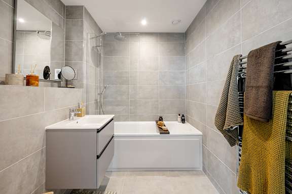 A modern bathroom with a white bathtub and a grey cabinet.