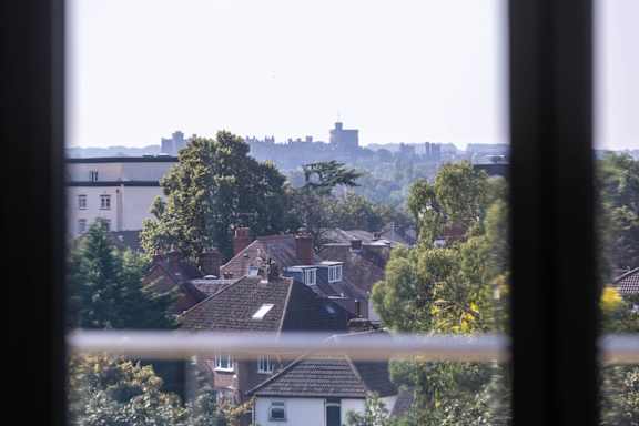 A view of a castle through a window with houses in the foreground.