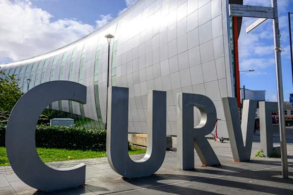 A large white letter C is in front of a glass building.