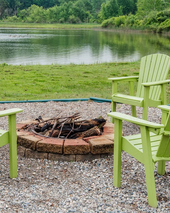 two green chairs sitting around a fire pit near a lake