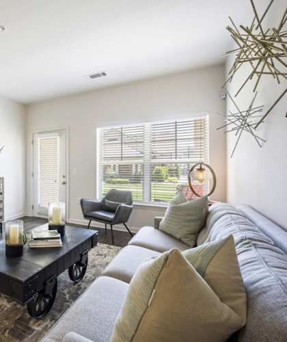 A living room with a grey couch, a coffee table, and a painting on the wall at The Maddox Apartments, Arkansas