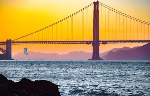 a view of the golden gate bridge at sunset with a kite surfer in the water