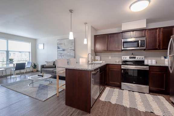 Kitchen area of an apartment fitted with a kitchen island, seating, stainless steel appliances, and spacious cabinets.