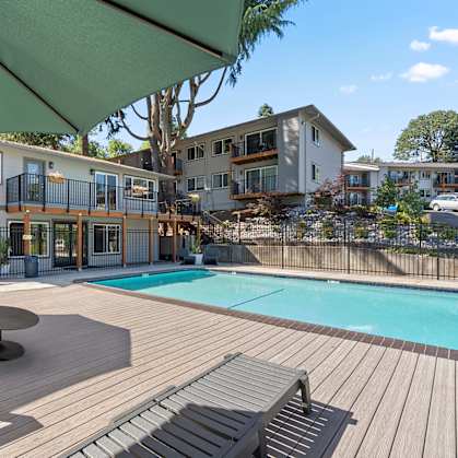 A wooden deck with a green umbrella over a pool.