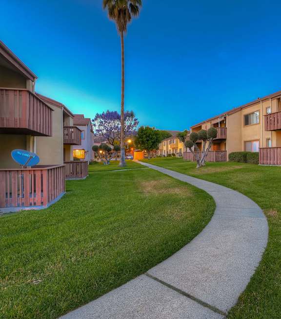 A pathway leads through a grassy area between two apartment buildings.