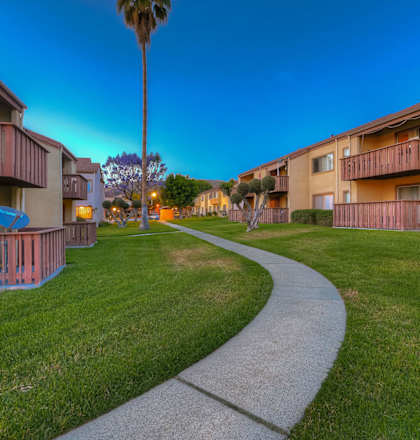 A pathway leads through a grassy area between two apartment buildings.