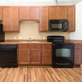 A black refrigerator, dishwasher, and oven in a kitchen with wooden cabinets.at Riverpoint Lofts, Iowa, 50309