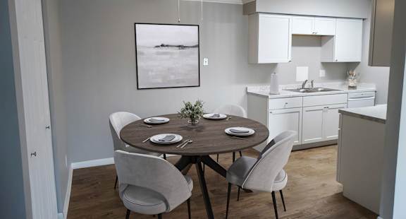 A dining room with a table set for two and a kitchen in the background.