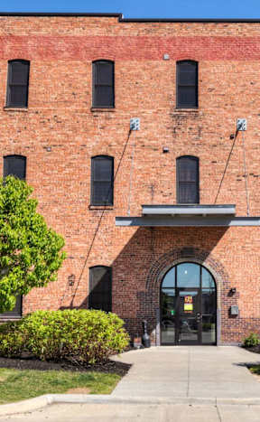 A red brick building with a large arched entrance and two trees in front.at Riverpoint Lofts, Des Moines, IA