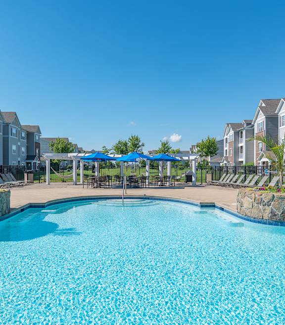 an outdoor pool with lounge chairs and umbrellas in front of an apartment building