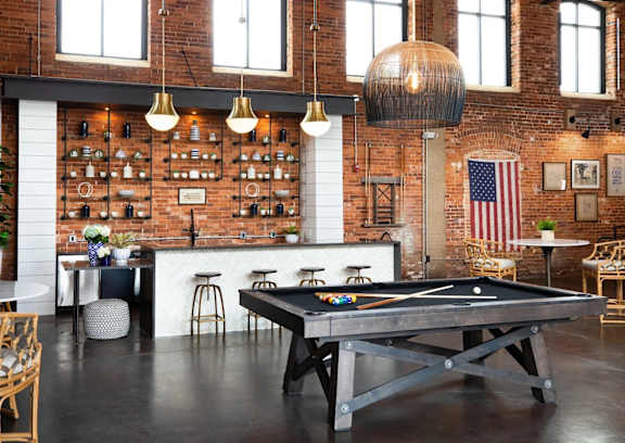 A pool table is in the middle of a room with a brick wall and a bar area.