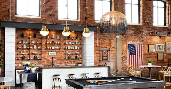 A pool table is in the middle of a room with a brick wall and a bar area.