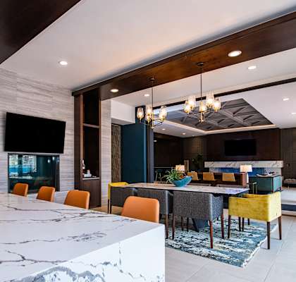 A modern kitchen with a marble countertop and a dining area with yellow chairs.
