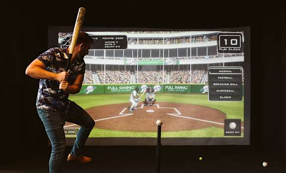 a man holding a baseball bat in front of a tv screen at The Apex at CityPlace, Overland Park, 66210