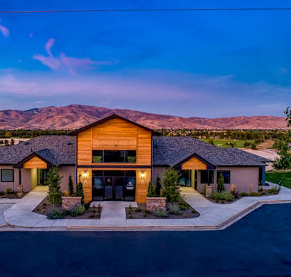 A modern house with a large front yard and a mountain range in the background.